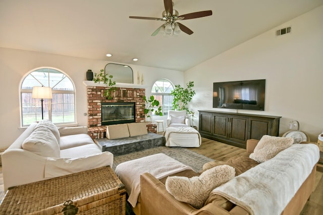 living area featuring visible vents, vaulted ceiling, a fireplace, wood finished floors, and a ceiling fan