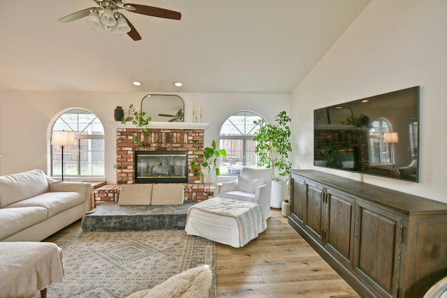 living room featuring a wealth of natural light, light wood finished floors, a brick fireplace, and vaulted ceiling