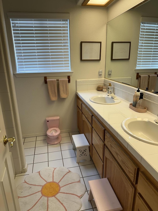 full bath featuring tile patterned floors, double vanity, baseboards, and a sink