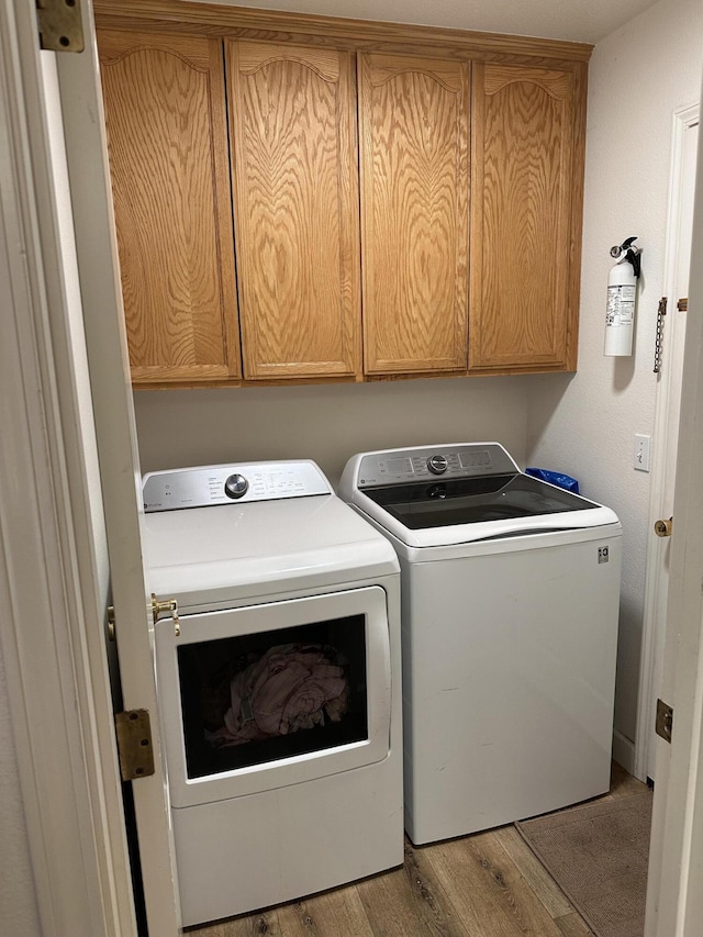 clothes washing area featuring washer and dryer, wood finished floors, and cabinet space