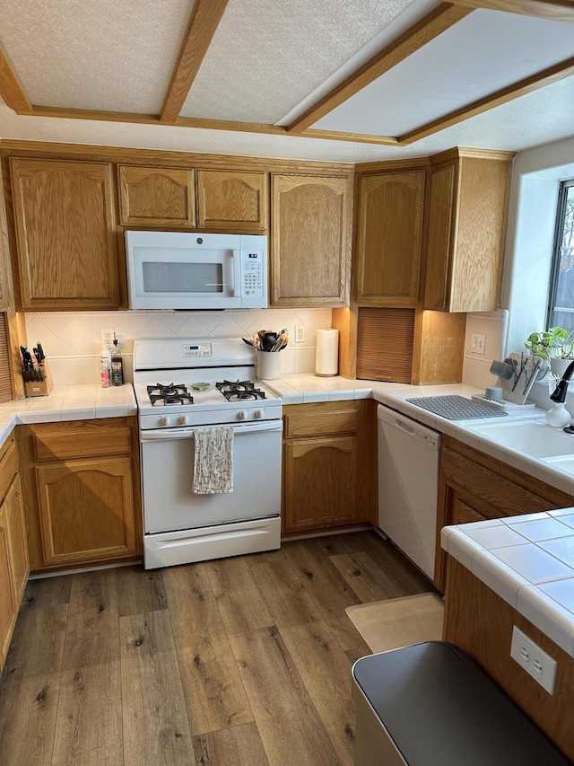 kitchen with decorative backsplash, white appliances, hardwood / wood-style flooring, and tile counters