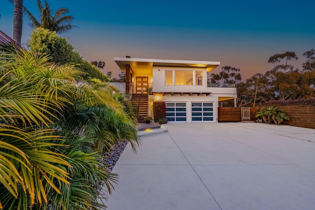 modern home featuring an attached garage, fence, stairs, stucco siding, and driveway