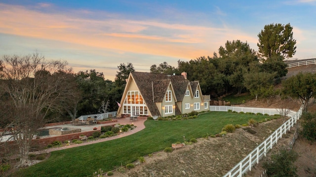 view of front of house featuring a patio area, a lawn, a fenced backyard, and a chimney