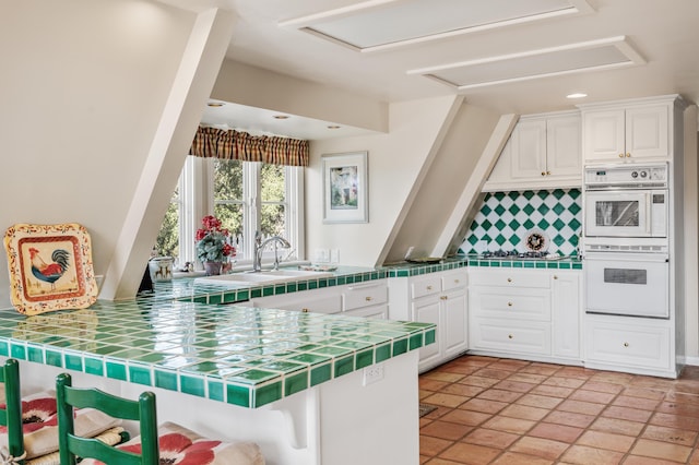 kitchen with backsplash, white double oven, tile countertops, white cabinets, and a sink