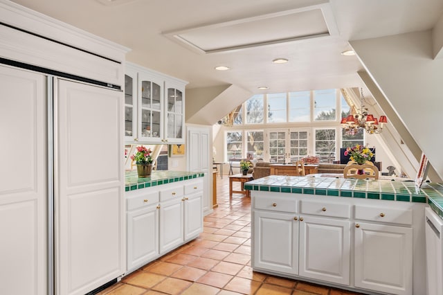 kitchen featuring glass insert cabinets, tile counters, vaulted ceiling, paneled built in refrigerator, and white cabinetry