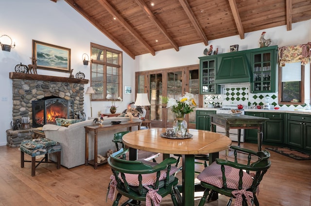 dining space featuring light wood-type flooring, beam ceiling, high vaulted ceiling, a stone fireplace, and wood ceiling