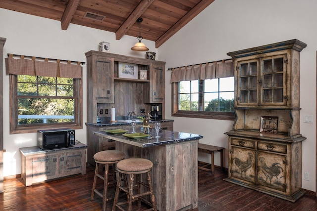 kitchen featuring a kitchen island, lofted ceiling with beams, black microwave, dark countertops, and wooden ceiling