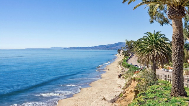 water view with a beach view, fence, and a mountain view