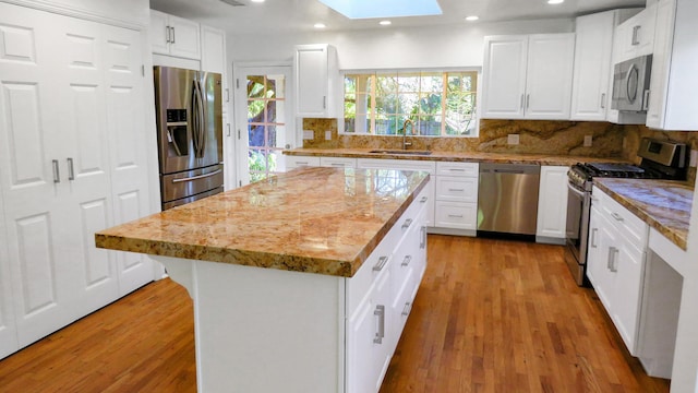 kitchen with light wood-type flooring, stainless steel appliances, backsplash, a sink, and a skylight