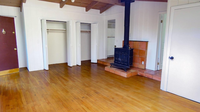 unfurnished bedroom featuring multiple closets, beam ceiling, light wood finished floors, and a wood stove