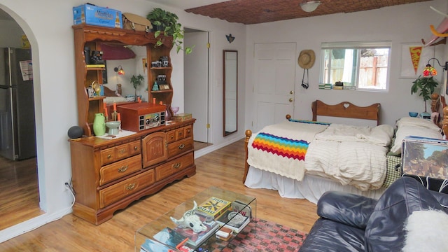 bedroom featuring freestanding refrigerator, light wood-style flooring, arched walkways, and baseboards