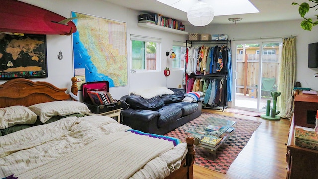 bedroom with access to exterior, wood finished floors, and a skylight