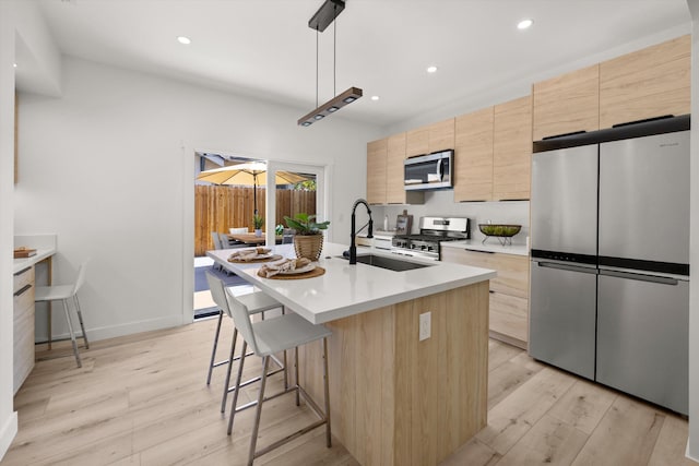 334 W Mission St, Santa Barbara, CA 93101 - kitchen featuring appliances with stainless steel finishes, light brown cabinets, a sink, light wood-type flooring, and a kitchen island with sink