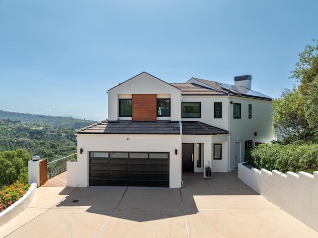 contemporary home with a chimney, solar panels, a garage, concrete driveway, and stucco siding