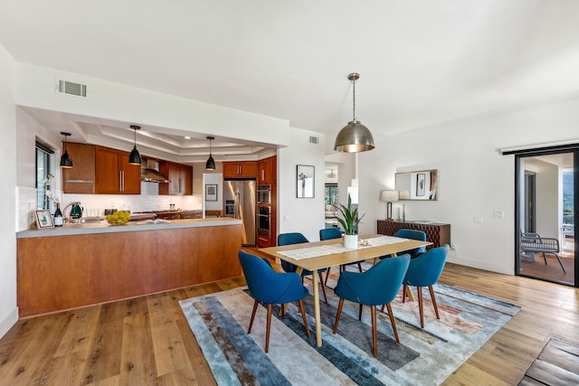 dining room with a tray ceiling, visible vents, and light wood-style flooring