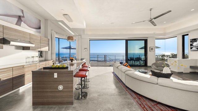 living area with a water view, ceiling fan, and concrete floors