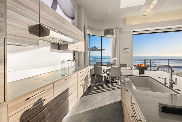 kitchen with modern cabinets, black electric stovetop, a water view, under cabinet range hood, and a sink