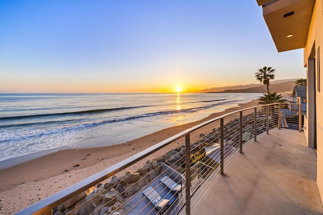 balcony at dusk featuring a water view and a view of the beach