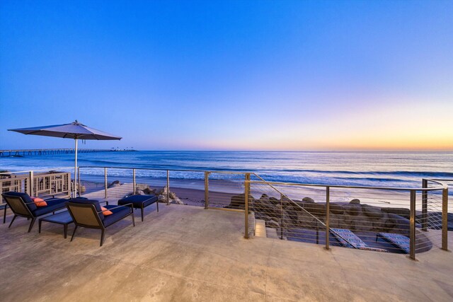 patio terrace at dusk with a water view, outdoor lounge area, and a view of the beach