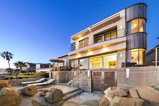 back of property with stucco siding, a balcony, and stairway