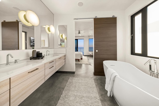 ensuite bathroom featuring double vanity, a sink, concrete floors, and a soaking tub