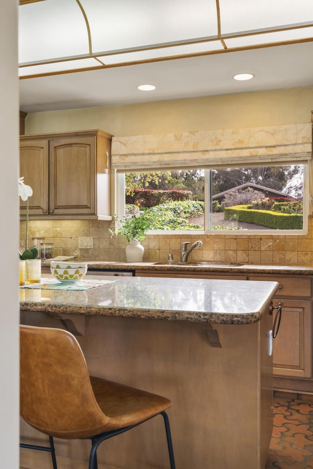 kitchen featuring a kitchen bar, recessed lighting, stone countertops, a sink, and decorative backsplash