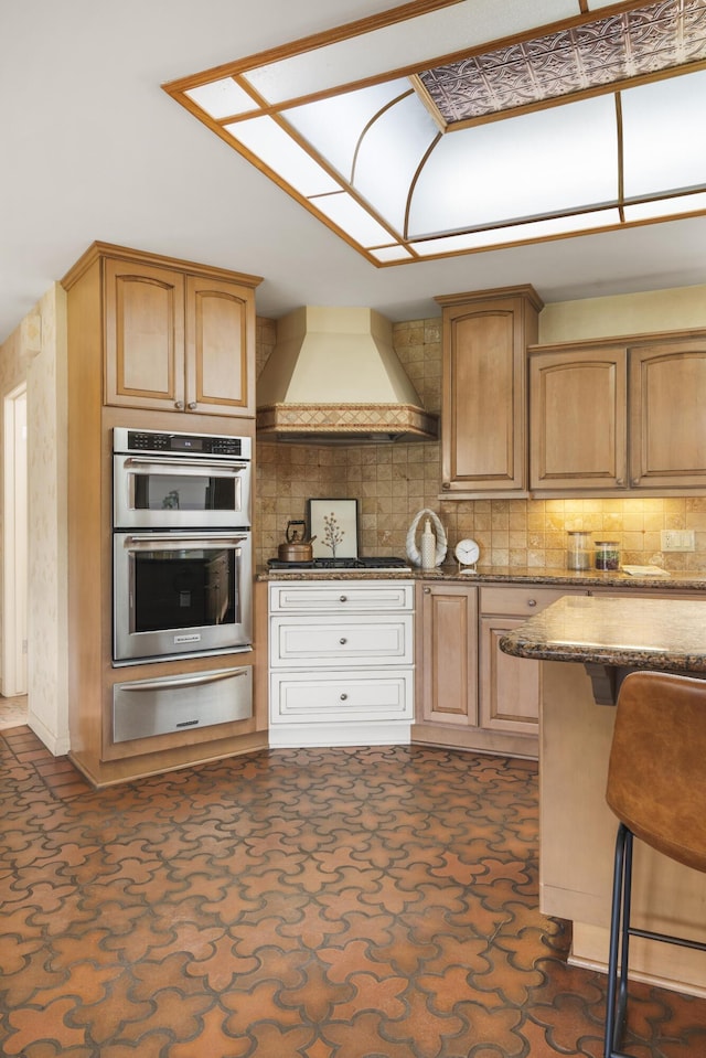 kitchen featuring custom range hood, a warming drawer, backsplash, dark stone counters, and appliances with stainless steel finishes