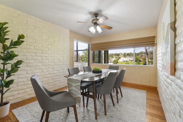 dining space with ceiling fan, light wood-type flooring, brick wall, and a healthy amount of sunlight