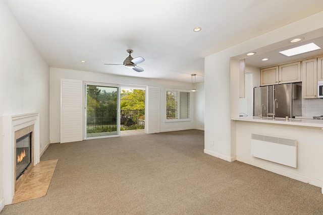 unfurnished living room featuring a fireplace, radiator, a ceiling fan, and carpet floors