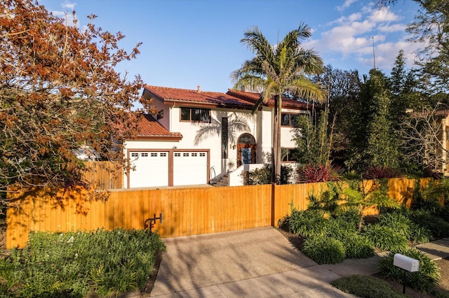 mediterranean / spanish house featuring a fenced front yard, a tiled roof, a garage, stucco siding, and a gate