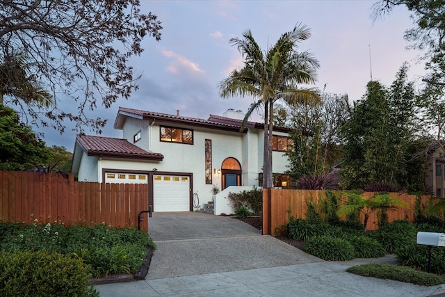 mediterranean / spanish home featuring a fenced front yard, a tile roof, stucco siding, and concrete driveway