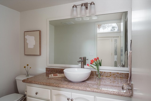 bathroom featuring toilet, vanity, backsplash, and visible vents