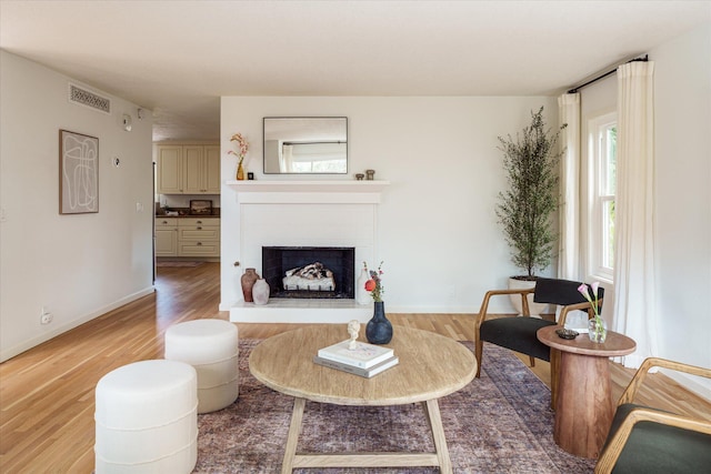 living area with a wealth of natural light, a fireplace with raised hearth, light wood-style floors, and visible vents