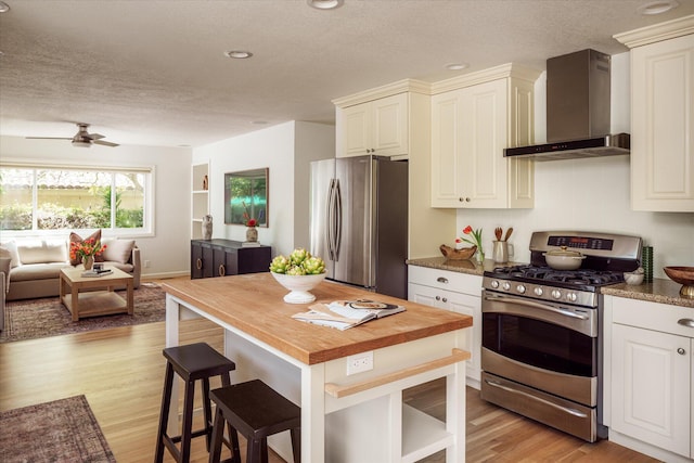 kitchen featuring wall chimney range hood, wood counters, a textured ceiling, and appliances with stainless steel finishes