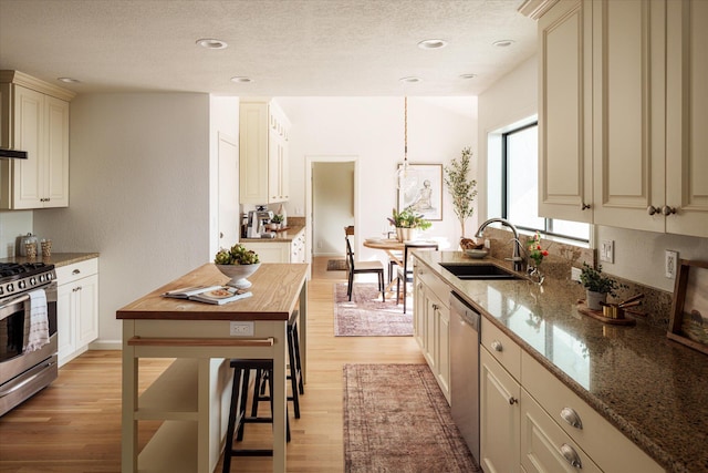 kitchen with wooden counters, appliances with stainless steel finishes, a textured ceiling, cream cabinetry, and light wood-style flooring