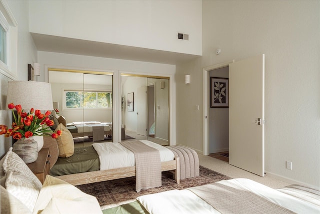 bedroom featuring a towering ceiling, visible vents, carpet floors, multiple closets, and baseboards