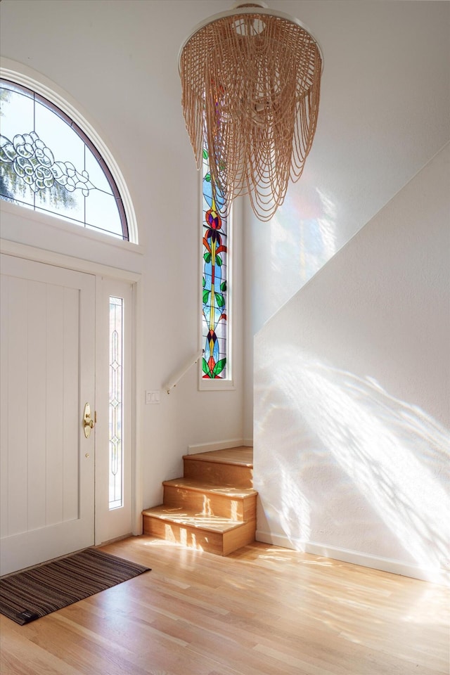 foyer entrance featuring a high ceiling, a notable chandelier, wood finished floors, and a healthy amount of sunlight