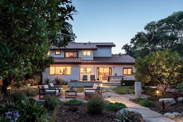 back of house at dusk featuring a patio area, stucco siding, an outdoor hangout area, and a tile roof