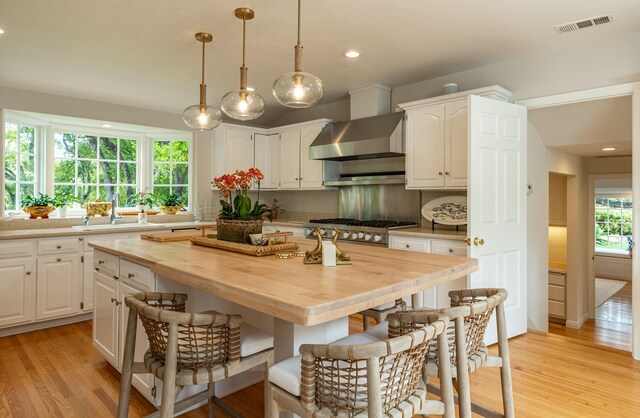 935 Arcady Rd, Santa Barbara, CA 93108 - kitchen featuring butcher block countertops, visible vents, wall chimney exhaust hood, a breakfast bar area, and a sink