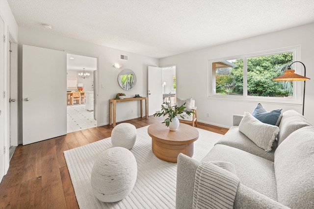 living room with a chandelier, visible vents, wood finished floors, and a textured ceiling