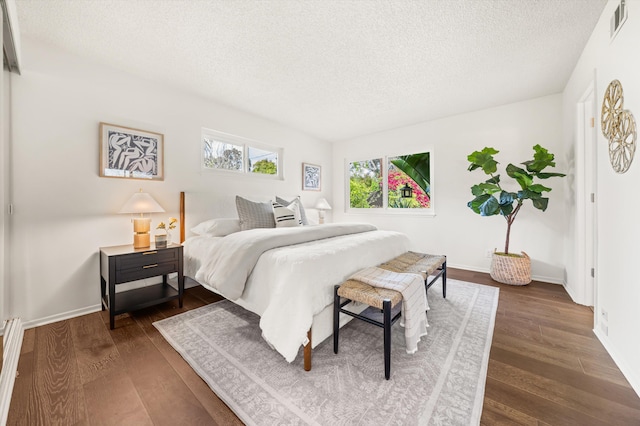 bedroom with dark wood-style floors, a textured ceiling, visible vents, and baseboards