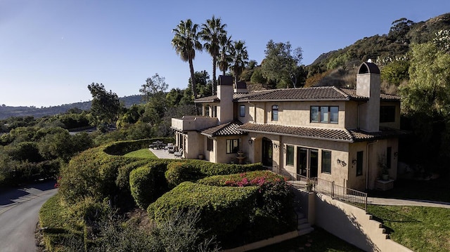 view of front of property featuring a tile roof, fence, stucco siding, and a chimney