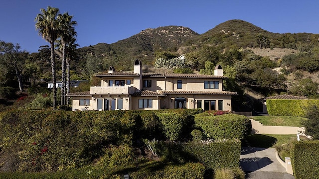 view of front facade with a tiled roof, a chimney, a mountain view, and stucco siding