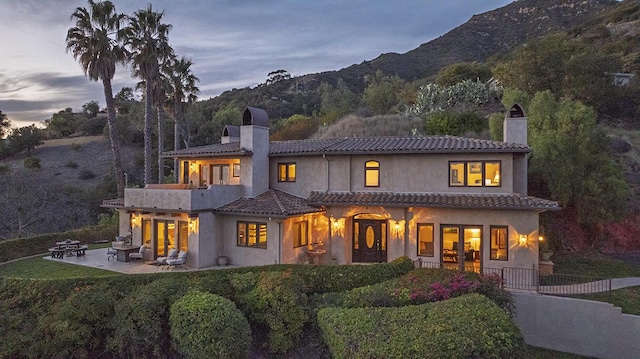 back of house with a mountain view, a chimney, a patio area, and stucco siding