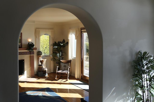 interior space with arched walkways, a tiled fireplace, ornamental molding, and wood finished floors