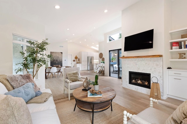 living room featuring a tiled fireplace, high vaulted ceiling, light wood-style floors, and recessed lighting