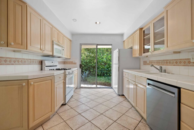 kitchen with glass insert cabinets, light brown cabinets, white appliances, tile counters, and decorative backsplash