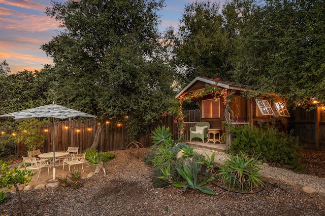yard at dusk featuring a fenced backyard, an outdoor structure, and a patio
