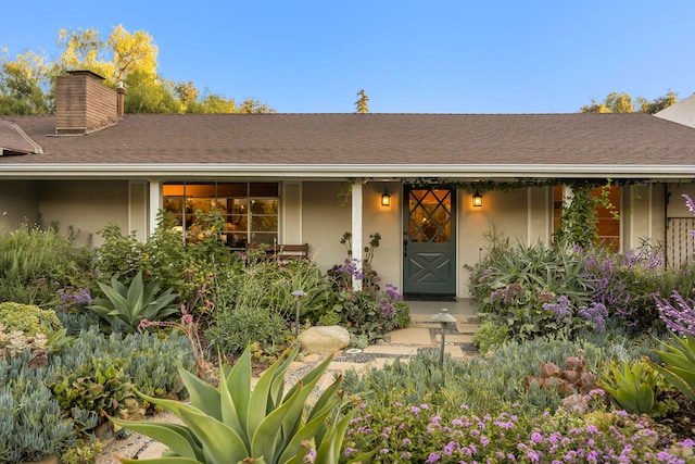 entrance to property featuring stucco siding, a chimney, and covered porch