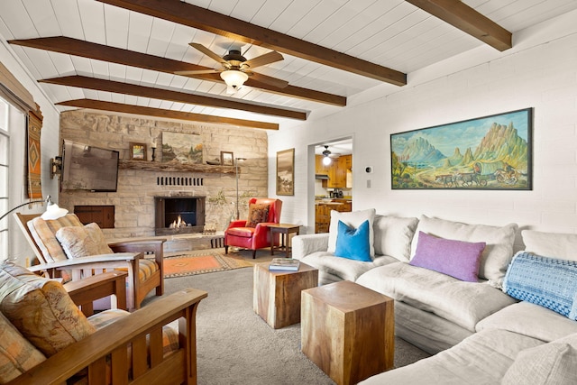 carpeted living room with beamed ceiling, a stone fireplace, a ceiling fan, and wooden ceiling